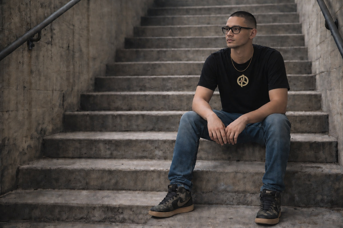 Bad Object OBJECT 001 small high-centre print on a black T-shirt, worn by the seated male model on concrete stairs.